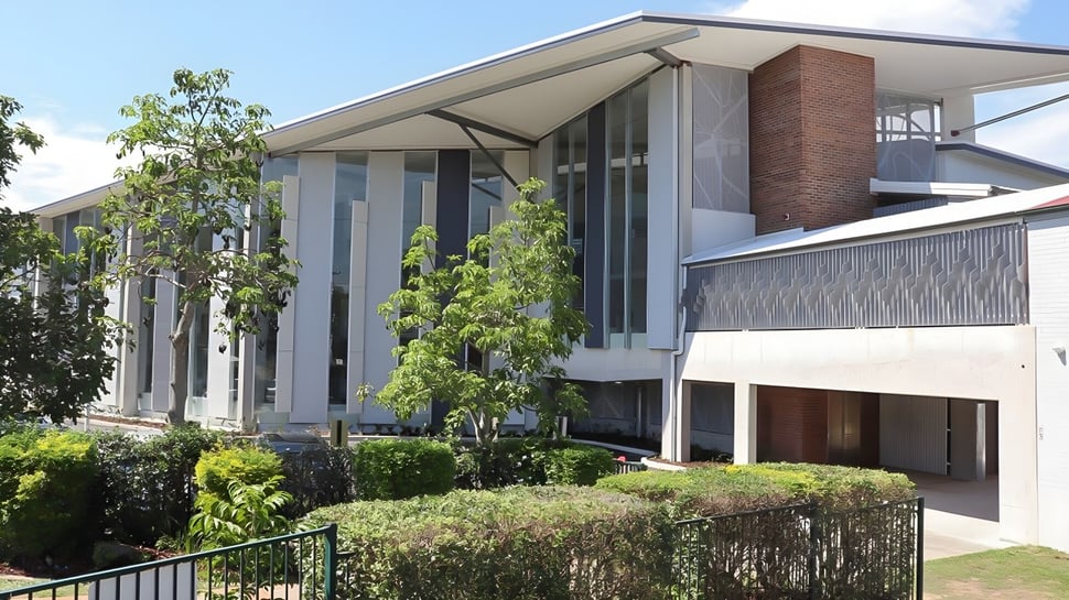 El moderno edificio de varios pisos con grandes ventanas y balcón en el campus de la The Gap State High School está rodeado de exuberante vegetación.