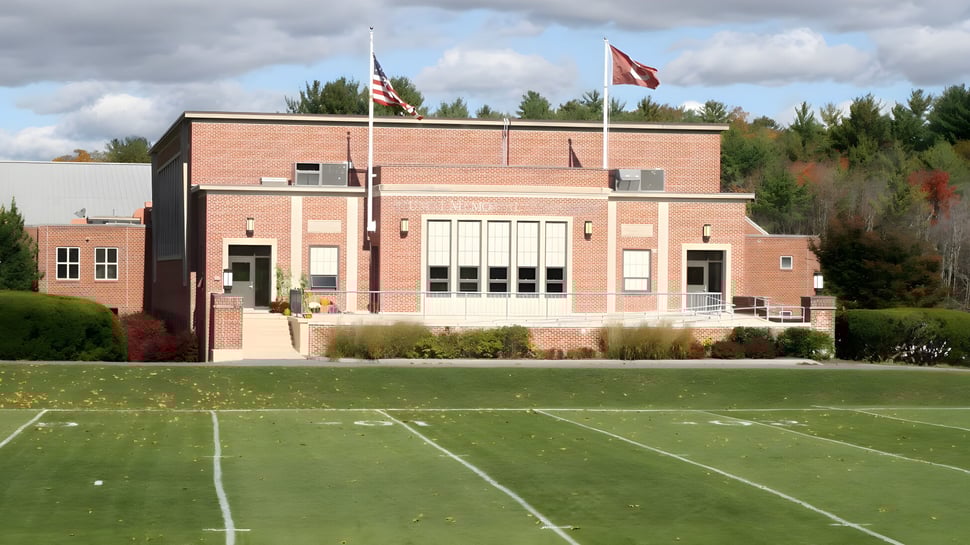 El edificio de ladrillo de The Governor's Academy con grandes ventanas y la bandera americana al fondo detrás de un campo.