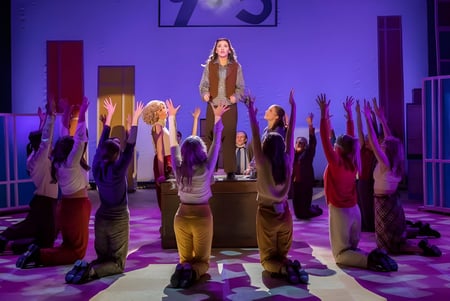 Un grupo de estudiantes está de pie con los brazos en alto en un pasillo de The Hammond School bajo luz violeta.