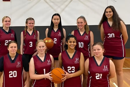 Un grupo de jóvenes estudiantes con uniformes burdeos posan con balones de baloncesto en la cancha de baloncesto de The Heights School.