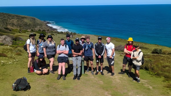 Un grupo de estudiantes de The Heights School está en una colina verde con vista al mar azul y la costa rocosa.