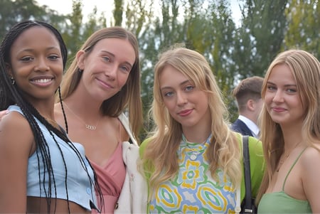 Cuatro estudiantes de The High School posan juntas sonriendo al aire libre frente a árboles y áreas verdes.