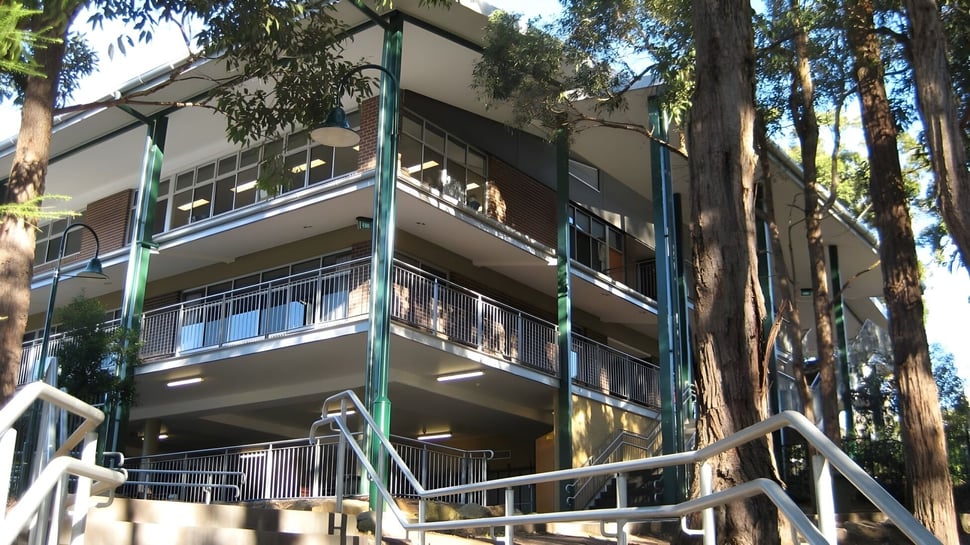El edificio de varios pisos de The Hills Grammar School con balcones está rodeado de altos árboles.