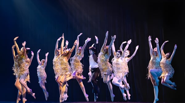Estudiantes de The King's Academy realizan una actuación de baile en el escenario con trajes brillantes.