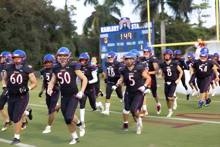 Un grupo de futbolistas en uniforme corre juntos en el campo de deportes de The King's Academy.