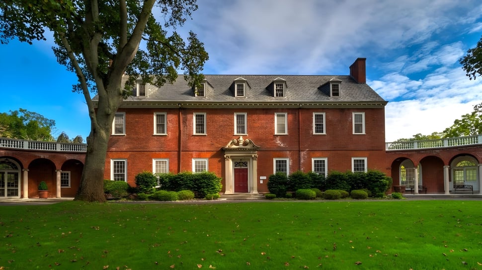 La mansión de The Knox School está rodeada de césped bien cuidado y altos árboles bajo un cielo azul.