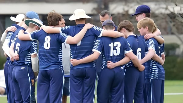 Un grupo de estudiantes de The Leys School está en el campo de deportes abrazándose mutuamente para apoyarse.