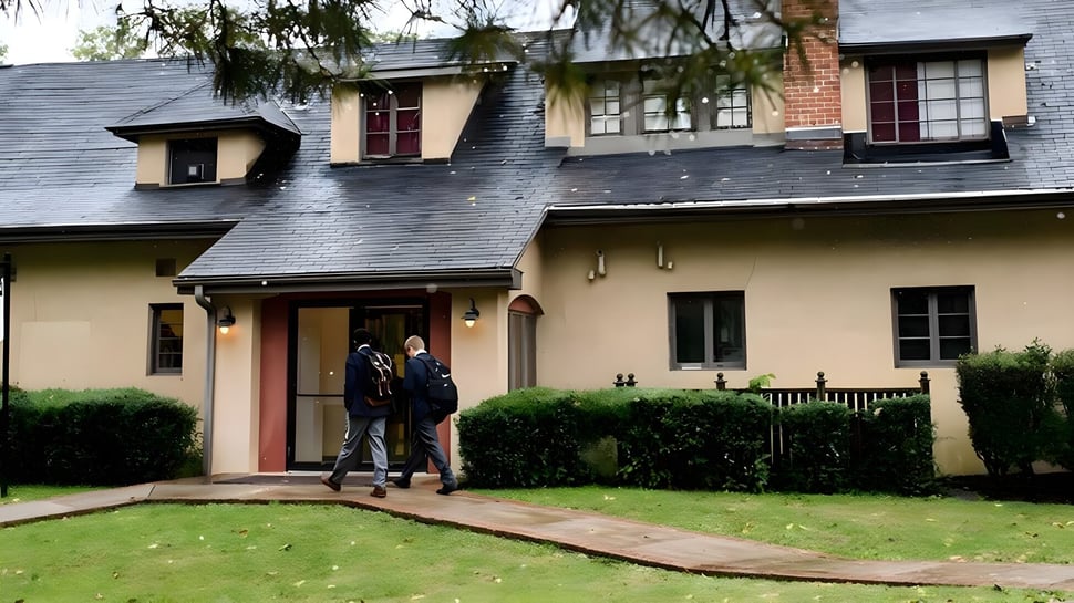 El edificio de ladrillo de dos pisos con veranda en el campus de The Linsly School con dos personas en la entrada.