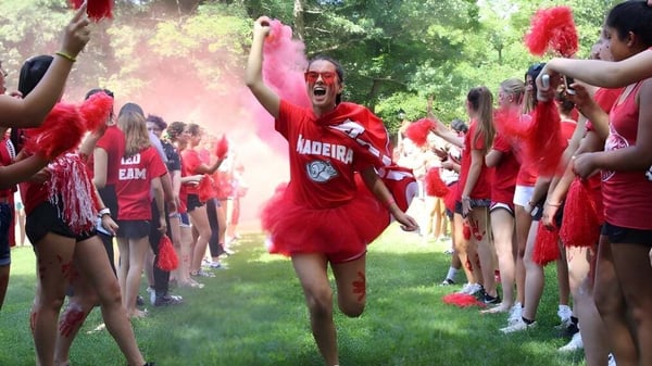 Un grupo de alumnas y alumnos en trajes rojos sostiene banderas en el terreno al aire libre de The Madeira School.