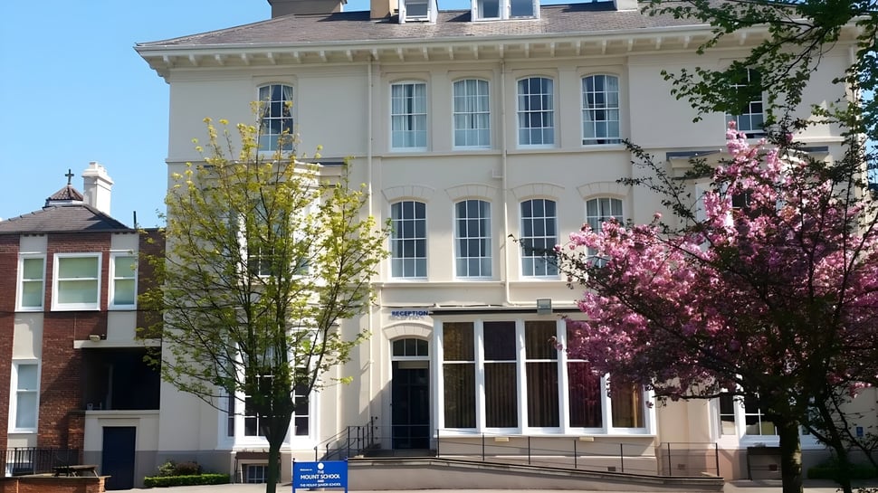 El edificio de varios pisos de The Mount School York está rodeado de árboles en flor y un cielo despejado.