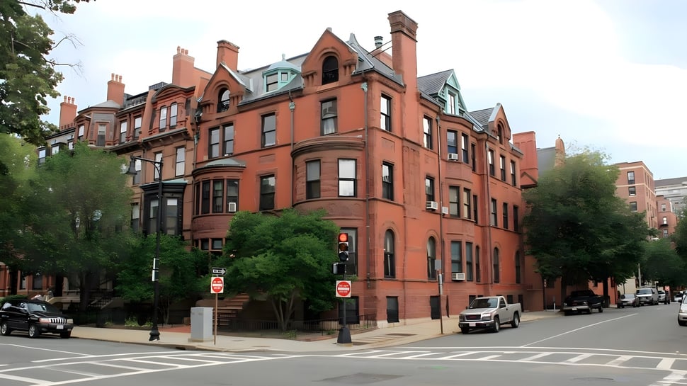 El edificio de ladrillo de varios pisos de The Newman School se encuentra en una calle de la ciudad y está rodeado de árboles y farolas.