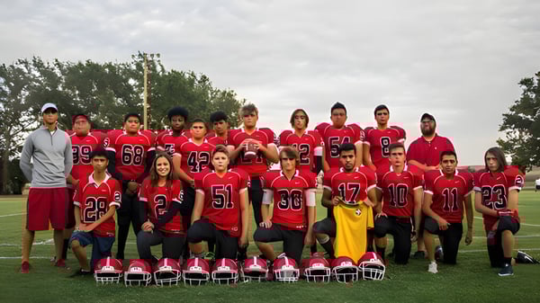 Un grupo de estudiantes de The Orme School está de pie en uniformes deportivos rojos y negros en un campo de césped con árboles de fondo.
