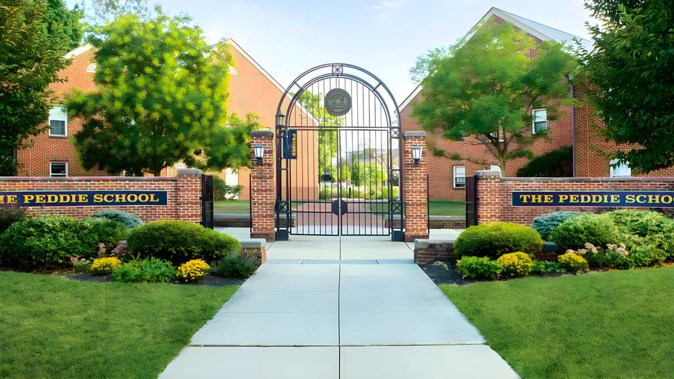 La entrada a The Peddie School con un arco de ladrillo y vista al cuidado campus con áreas verdes y edificios.