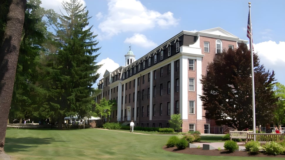 El gran edificio de ladrillo con torre en el campus de The Pennington School está rodeado de césped y árboles.