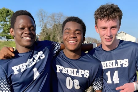 Tres estudiantes de The Phelps School llevan camisetas deportivas y están afuera frente a árboles y edificios.