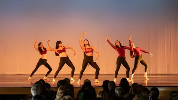 Un grupo de estudiantes de The Putney School realiza un baile en un escenario con trajes rojos y negros.