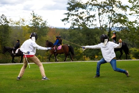 Dos personas en trajes de protección llevan caballos por un campo en el terreno de The Putney School.
