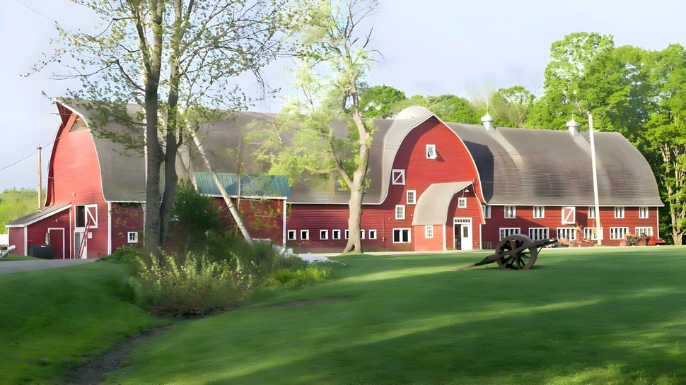 El edificio rojo del establo con un diseño especial en el campus de The Putney School rodeado de un paisaje verde.