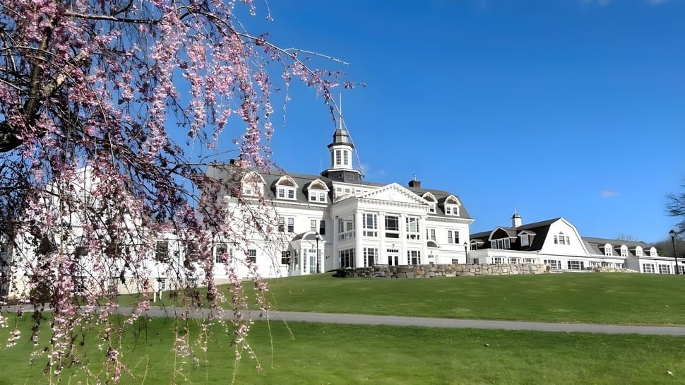 El histórico edificio principal de The Salisbury School se encuentra en un prado verde con cerezos en flor en primer plano.