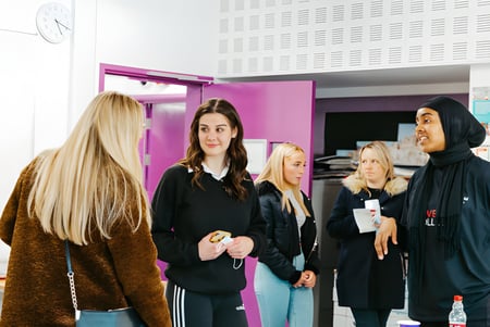 Un grupo de alumnas del The Sheffield College está en un pasillo con una pared rosa de fondo.