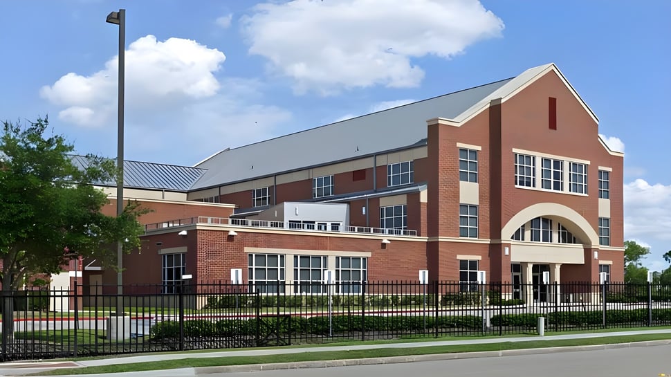 El edificio de ladrillo de varios pisos de The Village School con una entrada arqueada se encuentra en un área verde.