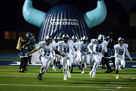 Estudiantes de The Village School corren en camisetas blancas hacia el campo frente a un gran casco vikingo inflable.