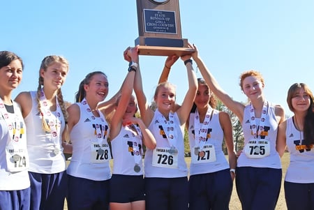 El equipo femenino de The Webb School sostiene juntos un trofeo bajo un cielo azul.