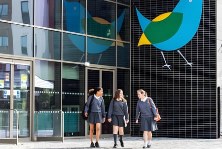 Tres estudiantes están frente a un edificio con grandes ventanas y un colorido mural en The Wren School.