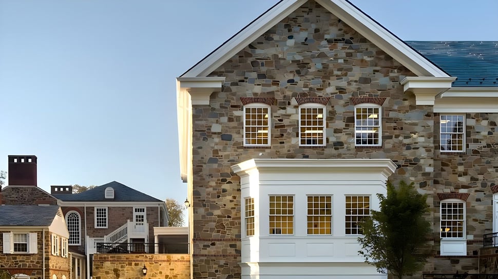El gran edificio de piedra de The Bryn Mawr School se encuentra frente a un cielo azul claro con edificios más pequeños al fondo.