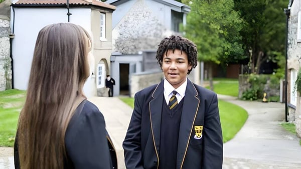 Dos estudiantes caminan juntos por un camino con áreas verdes y un edificio al fondo en el campus de la Thetford Grammar School.
