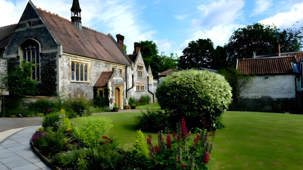 La iglesia de piedra con un jardín floreciente y una superficie de césped en el campus de la Thetford Grammar School.