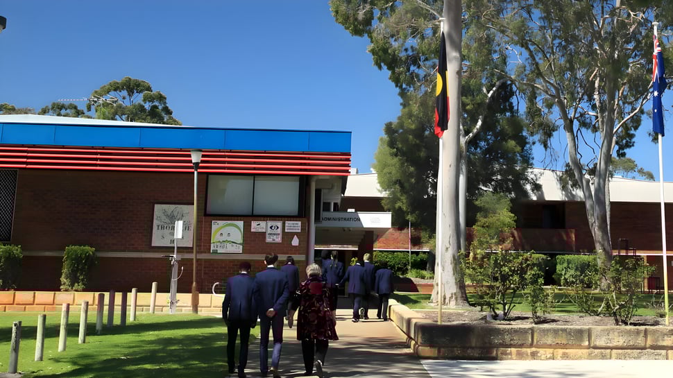 Un grupo de estudiantes camina por un camino cubierto de hierba hacia el edificio de ladrillo de la Thornlie Senior High School.