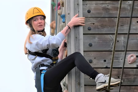 Una estudiante del Thornton College escala con casco en una estructura de madera.