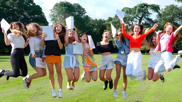 Un grupo de jóvenes estudiantes del Thornton College celebra juntas y salta en un área cubierta de hierba al aire libre.