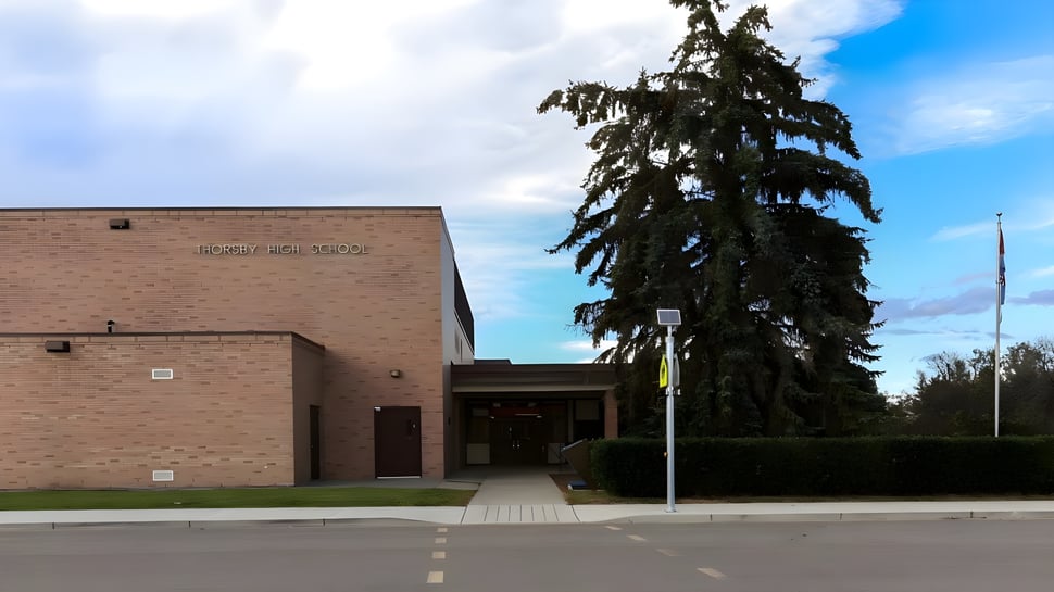 El edificio de ladrillo de la Thorsby Junior Senior High School con una gran entrada y un alto árbol de aguja en primer plano.
