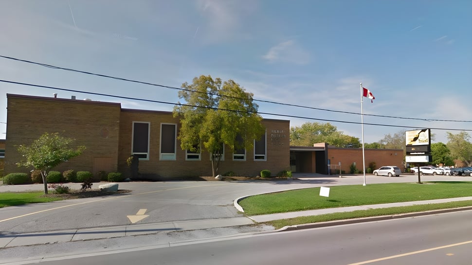 El edificio de ladrillo de la Tilbury District High School con una bandera canadiense en un asta y árboles alrededor.