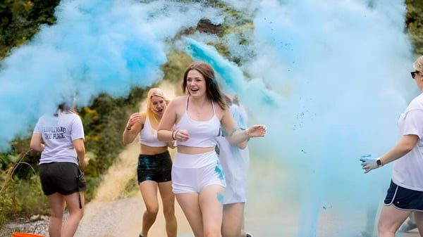 Un grupo de estudiantes de la Tilton School camina al aire libre a través de una nube de humo azul vibrante frente a un fondo verde.