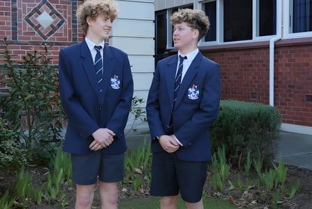 Dos estudiantes de la Timaru Boys School están frente a un edificio de ladrillo con ventanas en forma de diamante.