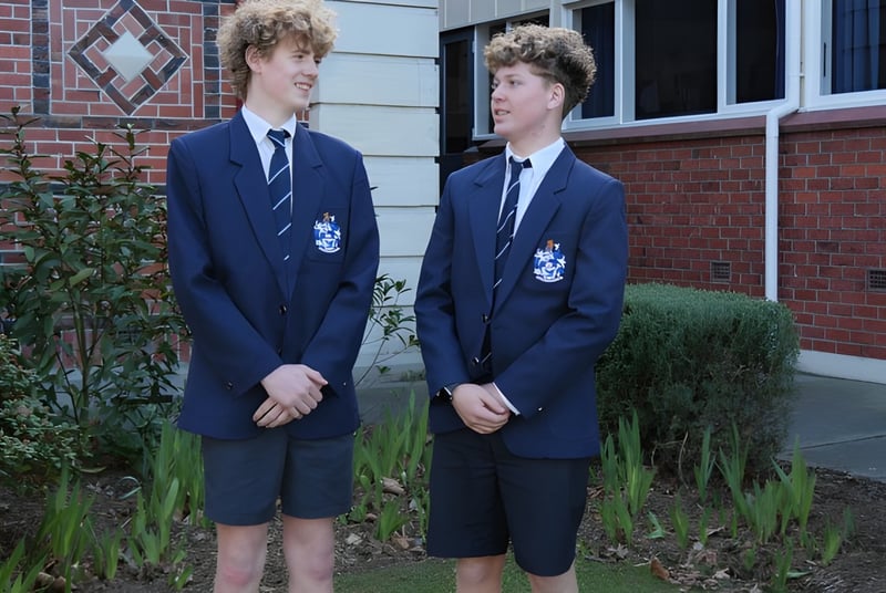 Dos estudiantes de la Timaru Boys School están frente a un edificio de ladrillo con ventanas en forma de diamante.