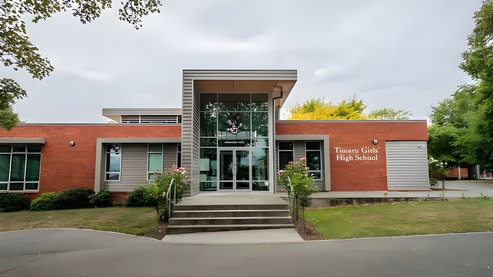 El moderno edificio en el campus de la Timaru Girls School está rodeado de árboles y una superficie de césped.