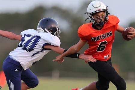 Dos futbolistas en camisetas rojas y azules juegan en el campo de la TMI Episcopal.