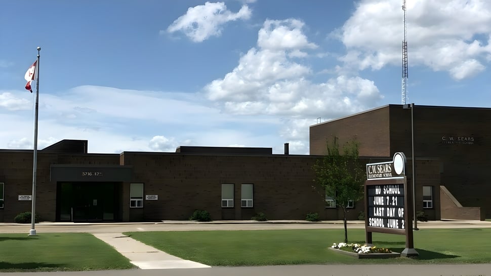 El edificio de ladrillo de Tofield School con una bandera canadiense y un área verde en el primer plano.