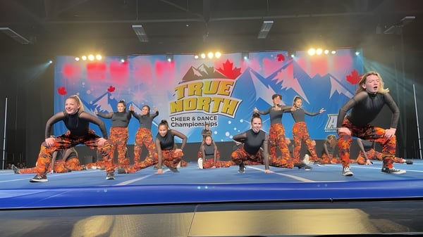 Un grupo de animadoras en uniformes coloridos realiza un espectáculo en el escenario con el banner del Tommy Douglas Collegiate.