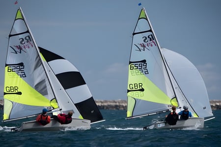 Dos veleros con bandera británica navegan bajo un cielo azul en el agua cerca de la Tonbridge School.