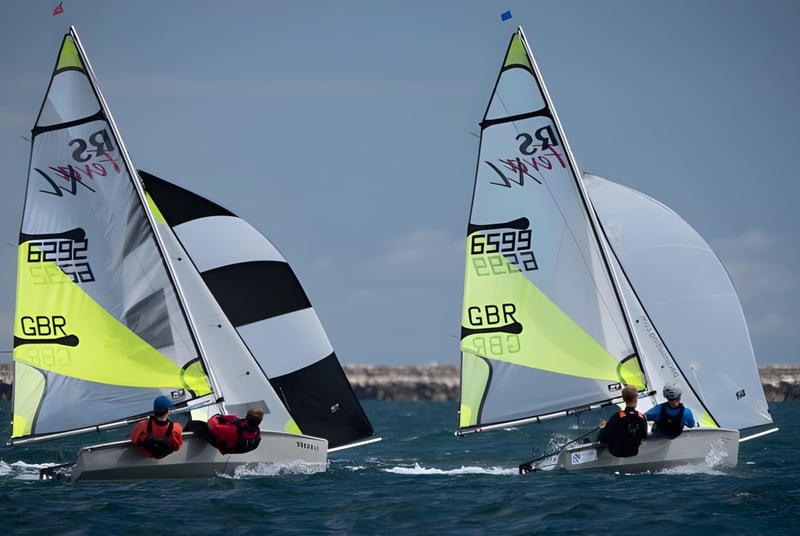 Dos veleros con bandera británica navegan bajo un cielo azul en el agua cerca de la Tonbridge School.