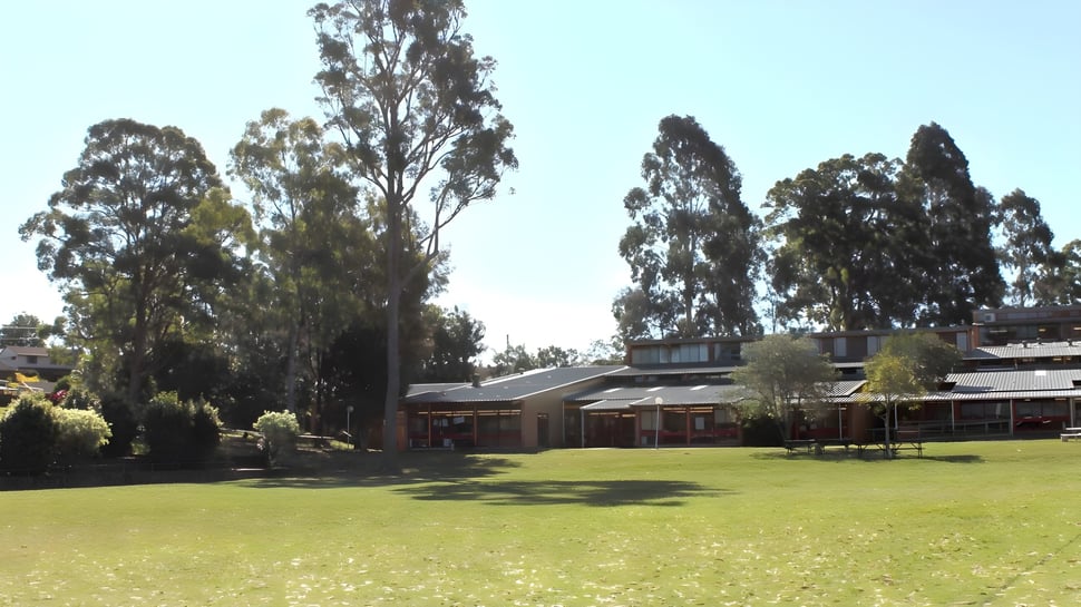 Una pradera verde con altos árboles y edificios al fondo en el terreno de la Toormina High School.