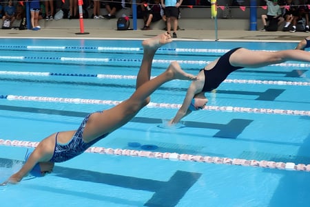 Un nadador en traje de baño negro se sumerge en la piscina en el terreno de la Toormina High School.