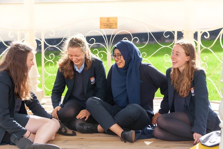 Cuatro alumnas de la Torquay Girls Grammar School están sentadas juntas en un banco frente a una puerta de metal decorativa.