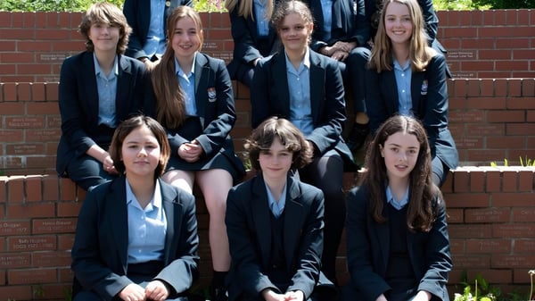 Un grupo de alumnas de la Torquay Girls Grammar School está de pie juntas frente a una pared de ladrillo.