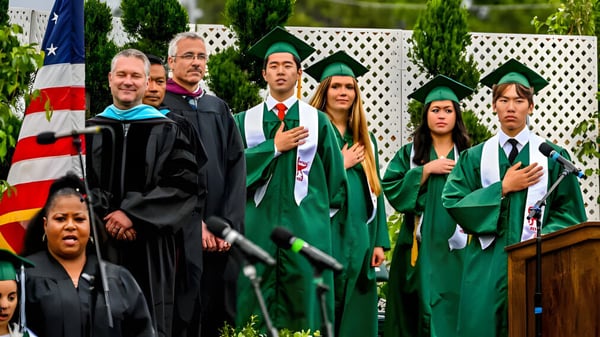 Los graduados de la Torrance South High School en togas verdes y negras están de pie frente a una bandera americana al aire libre.